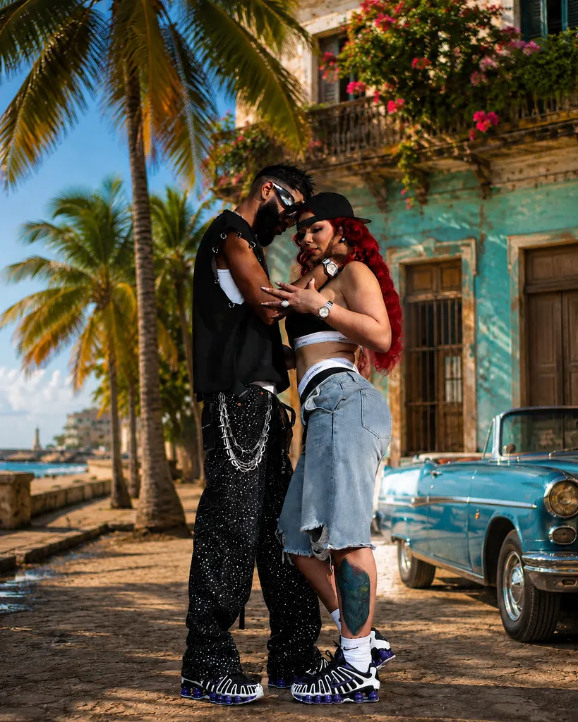 Anita Dieppa y El Yonki en una escena urbana caribeña con calle adoquinada, arquitectura colonial y auto clásico